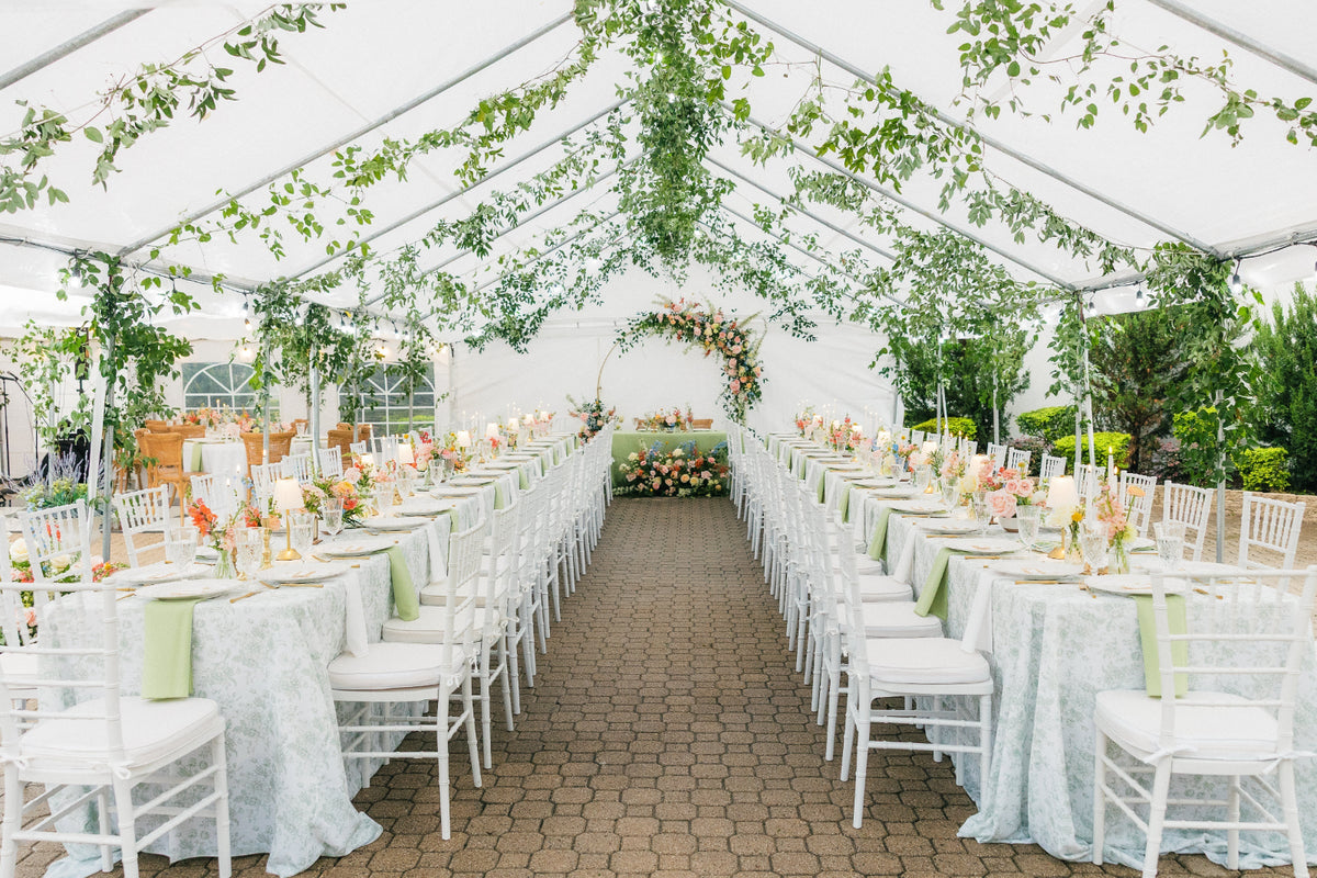 Tented reception with hanging greenery, long tables in pale linens and a floral arch at the far end