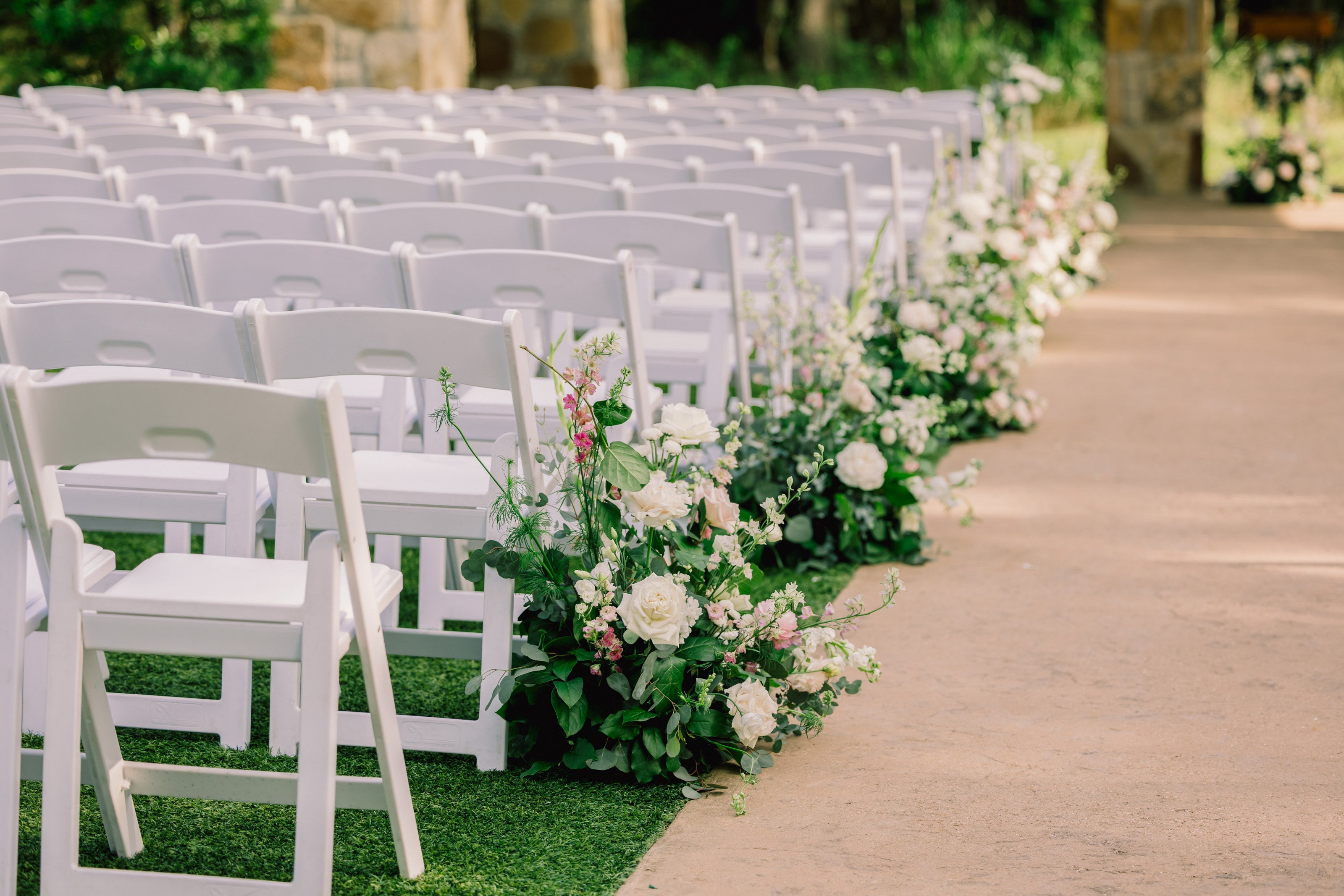 Pastel ceremony aisle at The Springs Alvarado with ground florals of white roses, snapdragons, and pink delphinium running the length of the path, by B.blumen