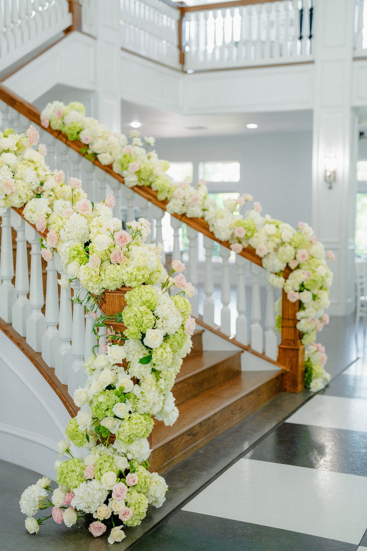 Garland of white and green hydrangea with blush roses cascading down a grand staircase rail