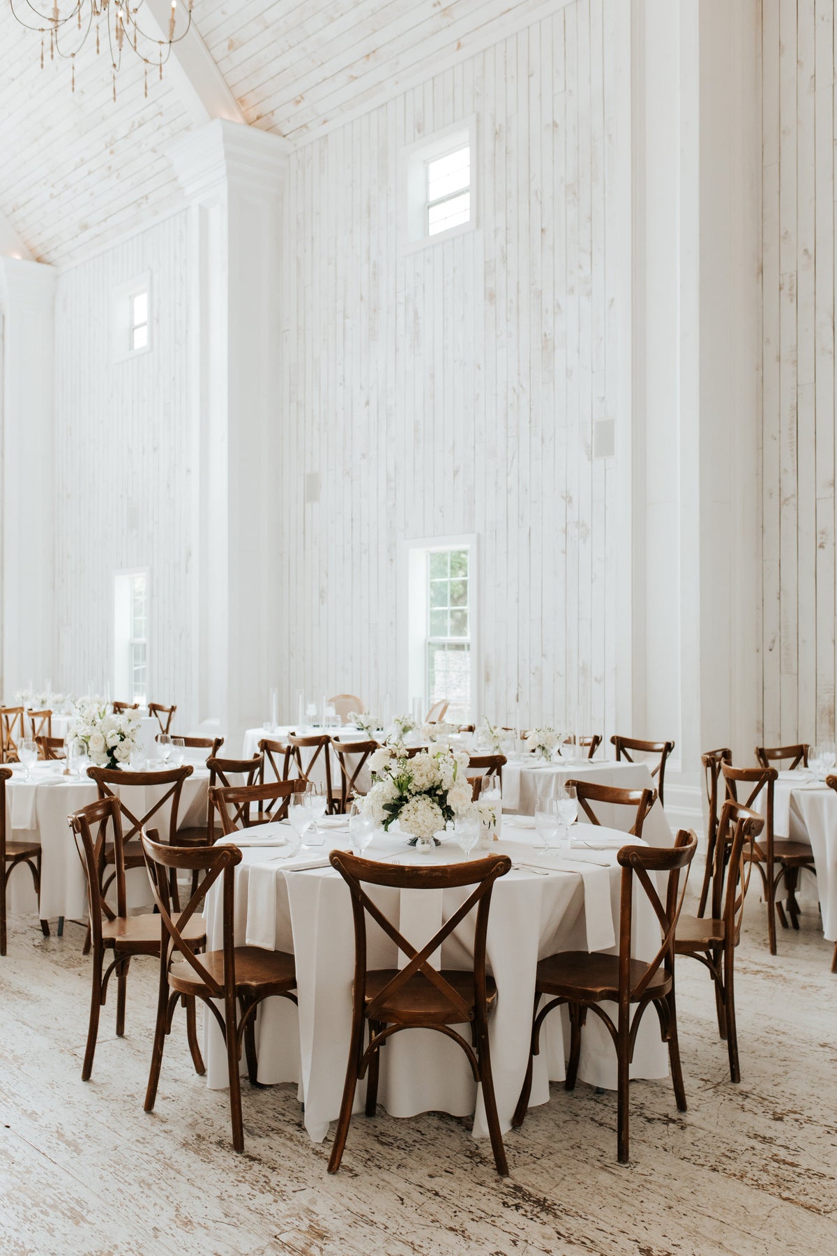 Round guest tables set with low pastel centerpieces in the white-walled reception room at The Springs White Sparrow.