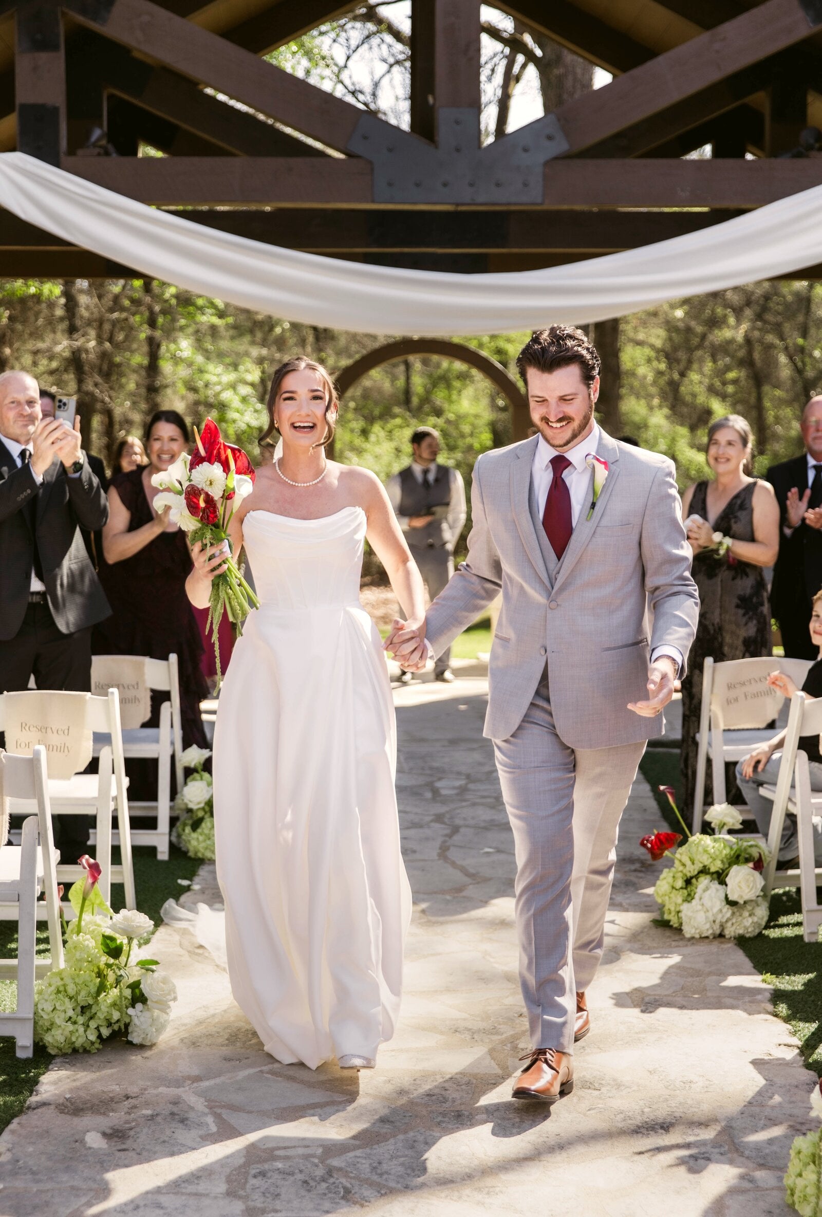 Bride and groom recessional under the Poetry Springs wood-beam pavilion with white ceremony drape billowing overhead, by B.blumen