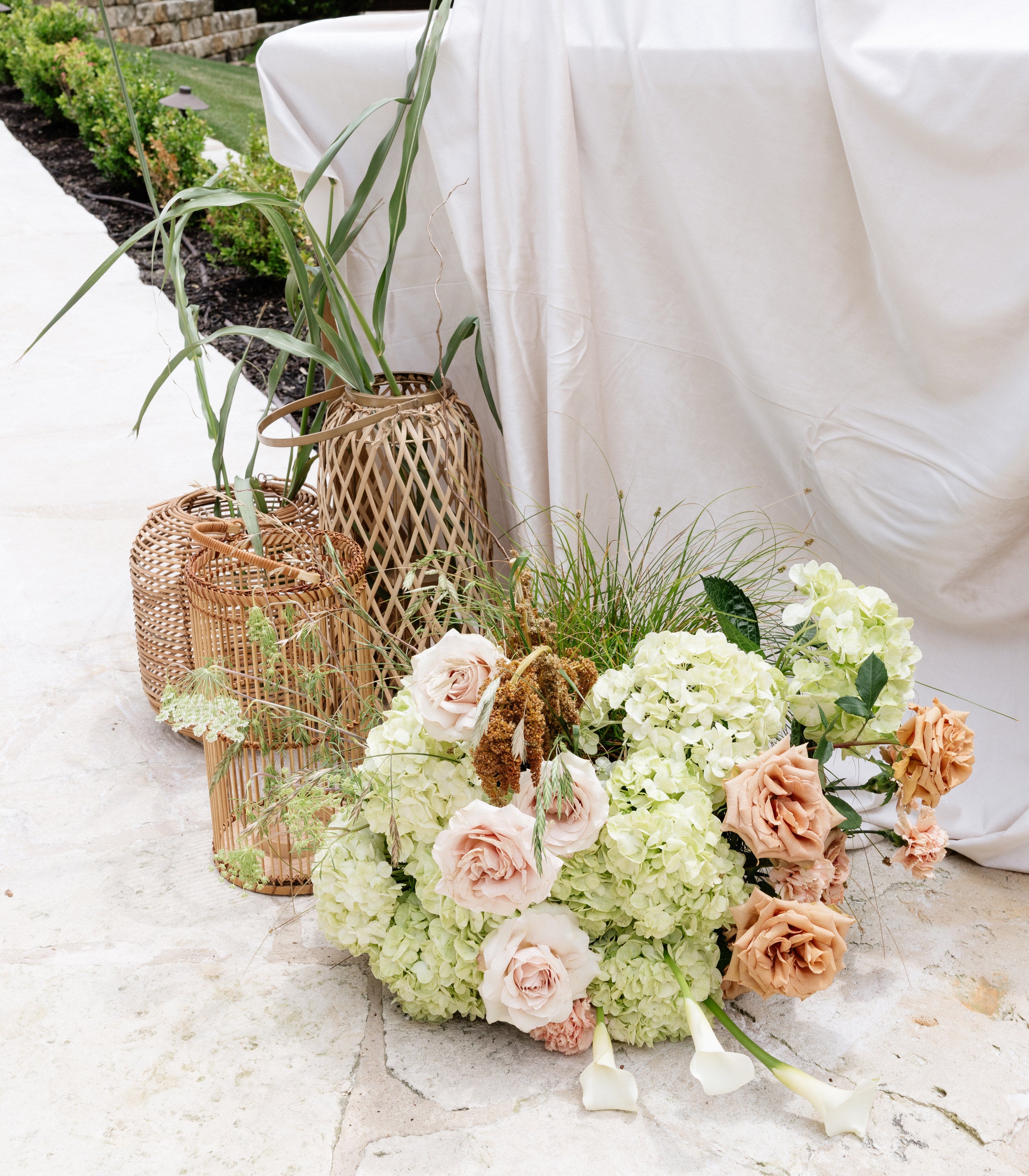 Ground arrangement at The Springs Rockwall in blush, cream and green with woven lanterns, set against white draped fabric, by B.blumen