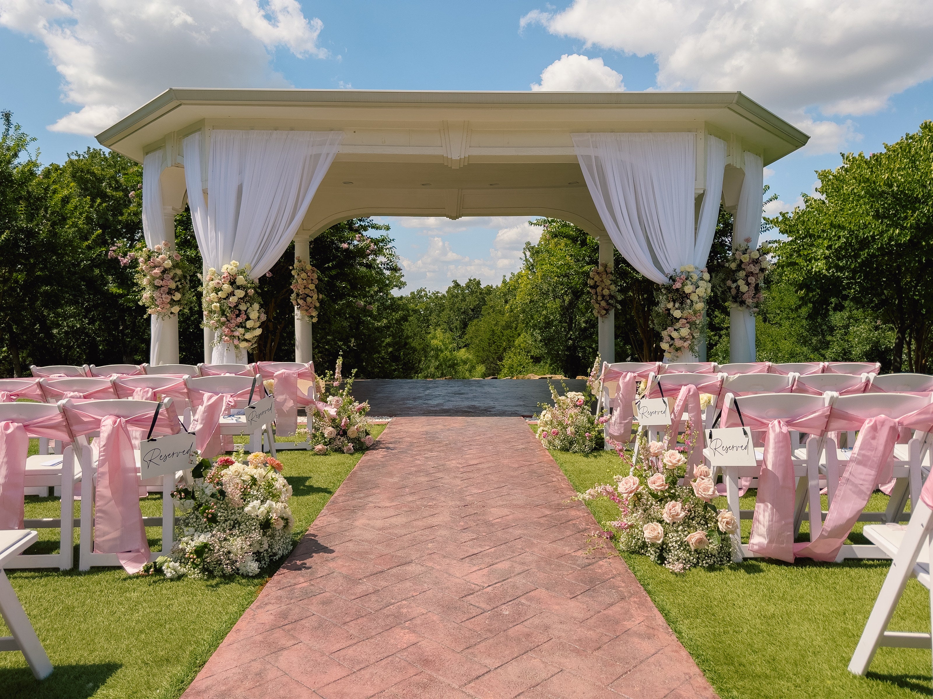 White pavilion ceremony at Parker Manor with drapes, pink chair ribbons, and a pastel floral aisle on the brick, by B.blumen