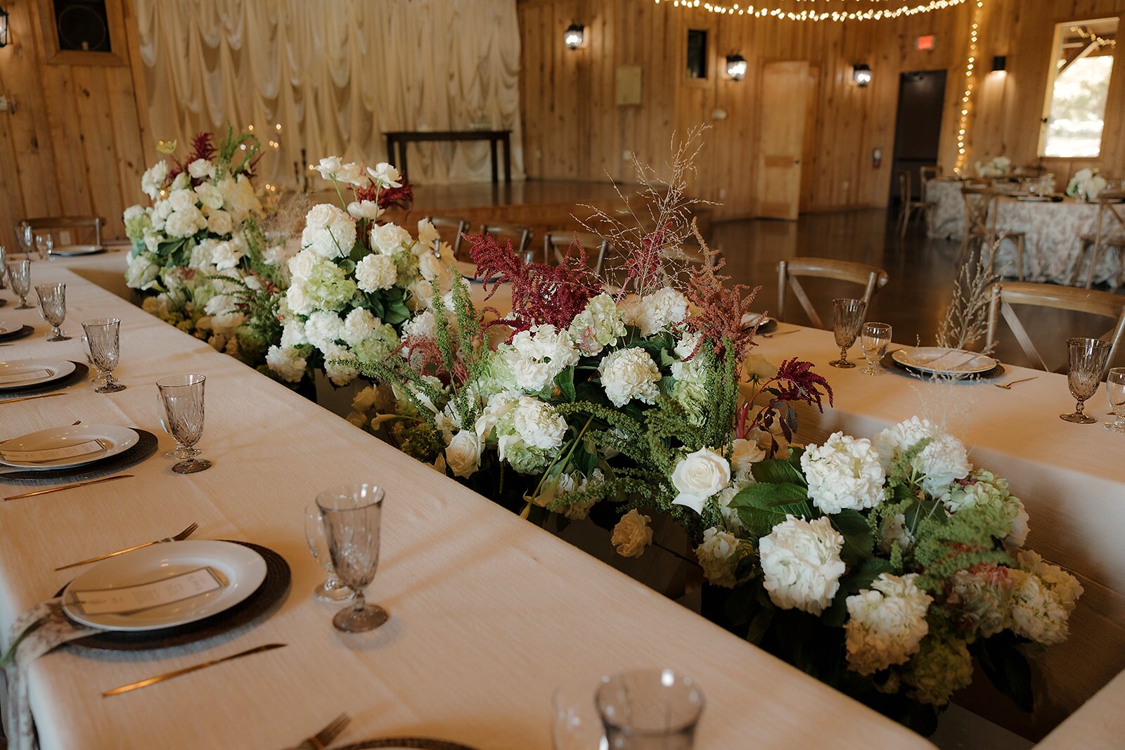 Continuous centerpiece run at Westwood Hall long table with white hydrangea, coral roses, red astilbe, and trailing greenery by B.blumen