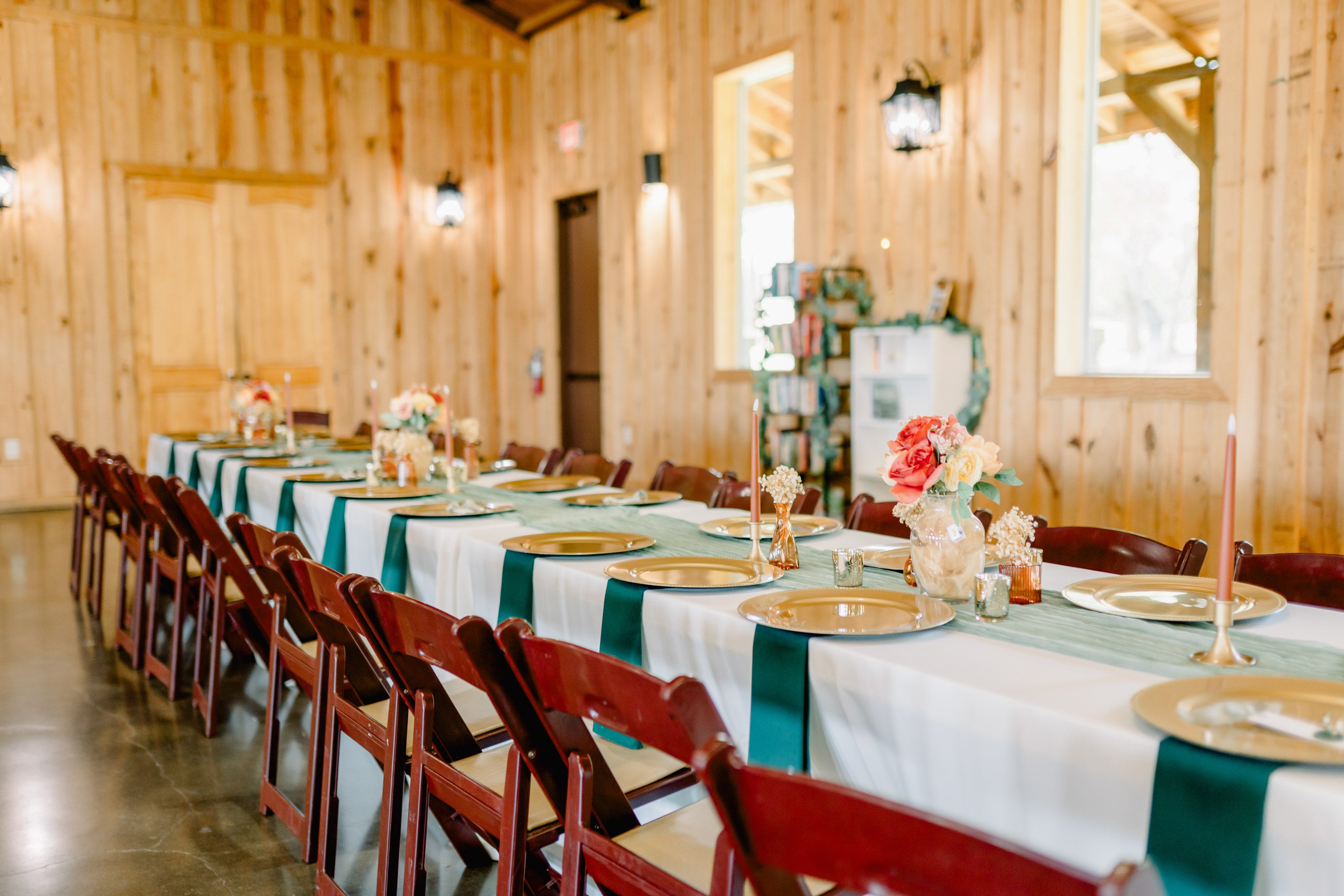 Long reception table at Westwood Hall with white centerpieces, teal sashes, gold chargers, and clustered candles, set against warm wood walls by B.blumen