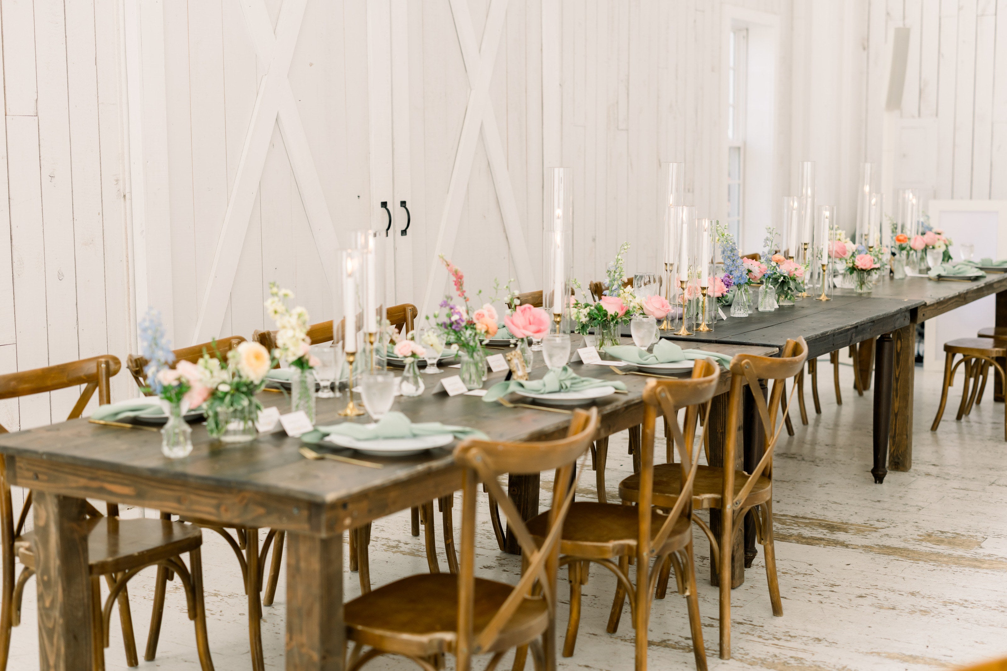 Long head table at The White Sparrow with a greenery runner, taper candles, and place settings down the run, cross-back chairs along both sides, by B.blumen