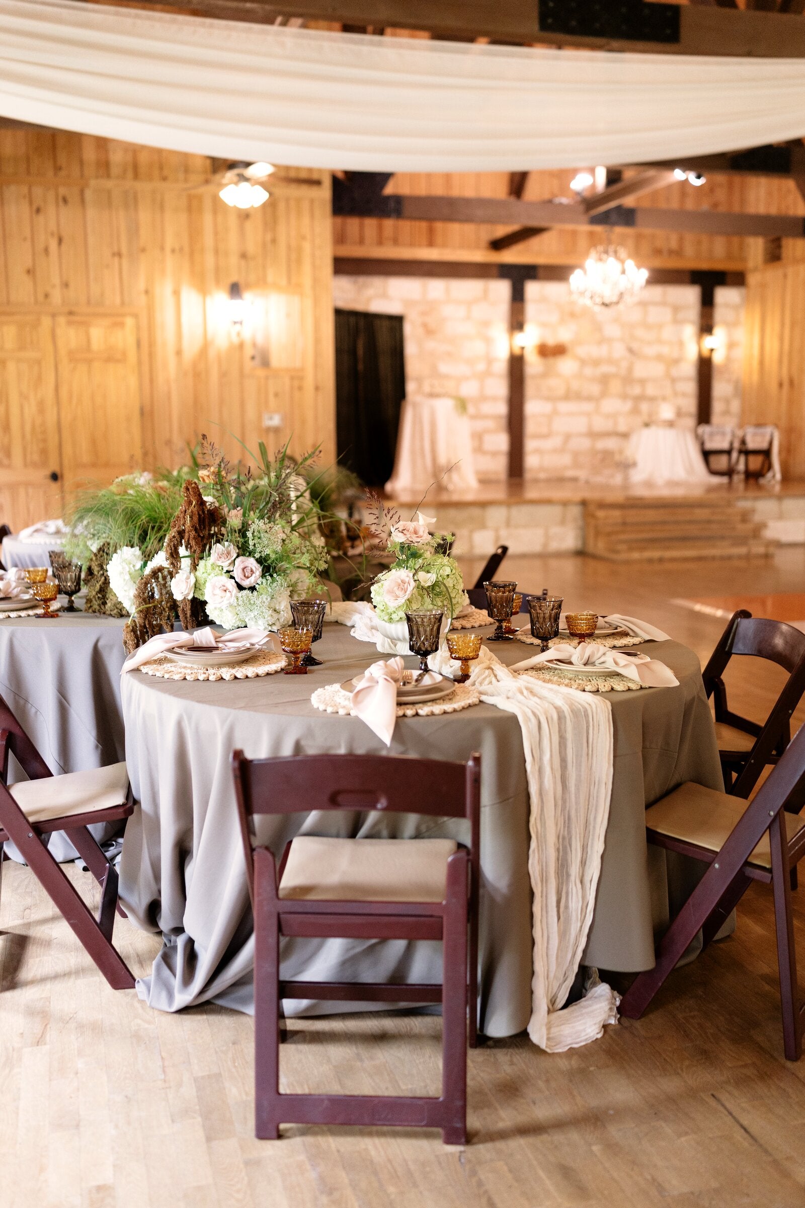 Round sweetheart-and-guest table setup at Poetry Springs with pastel florals, pampas, dried grasses, gray linen, and amber goblets, by B.blumen