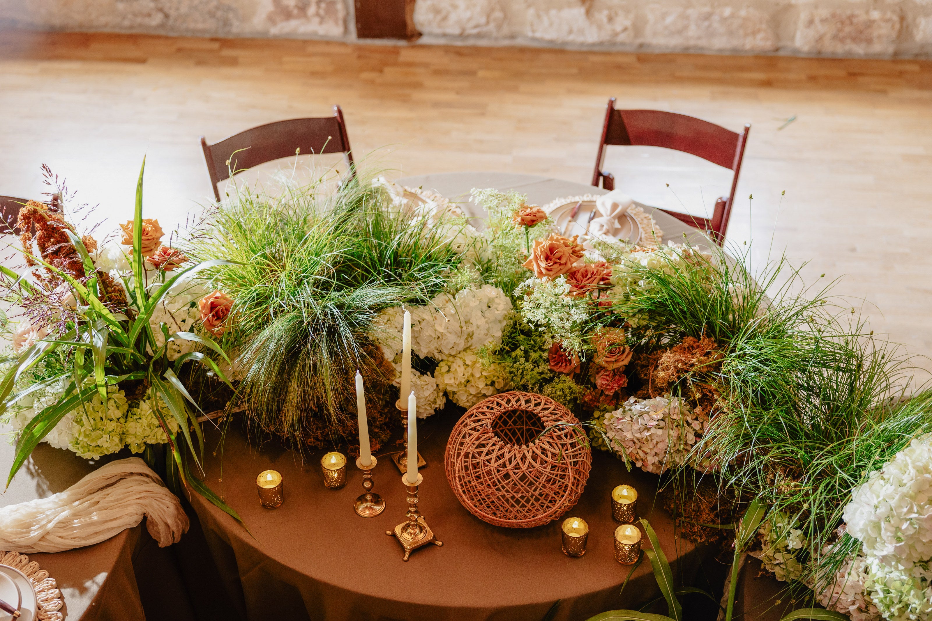Head table at Poetry Springs with a centerpiece garland of grasses, hydrangea, and peach roses among candlelight, by B.blumen