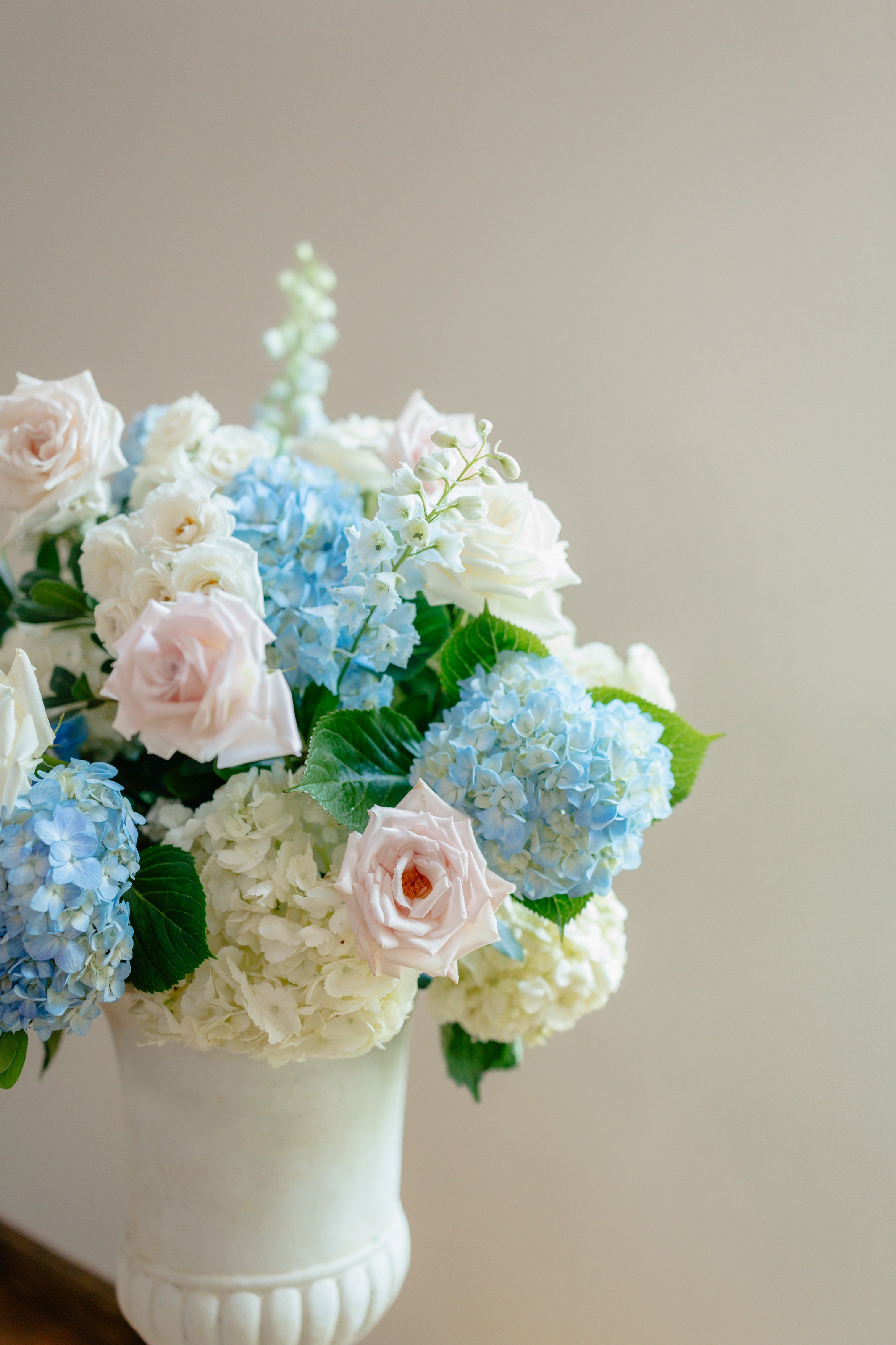 Urn arrangement of blue hydrangea, blush roses, and white delphinium at The Springs Waxahachie by B.blumen