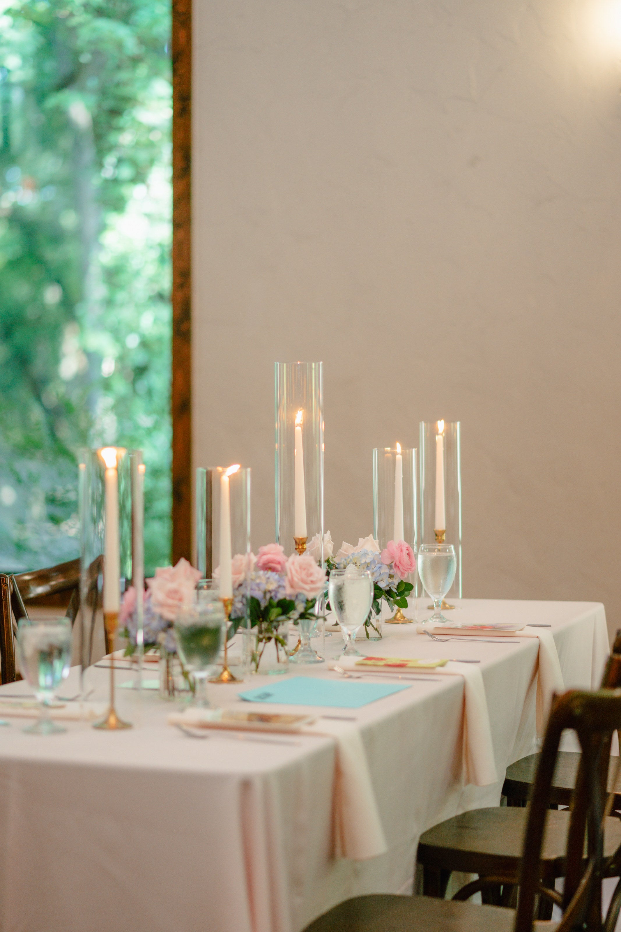 Candlelit head table at The Springs Waxahachie with peach linens, taper candles in glass, and low blush florals by the window, by B.blumen