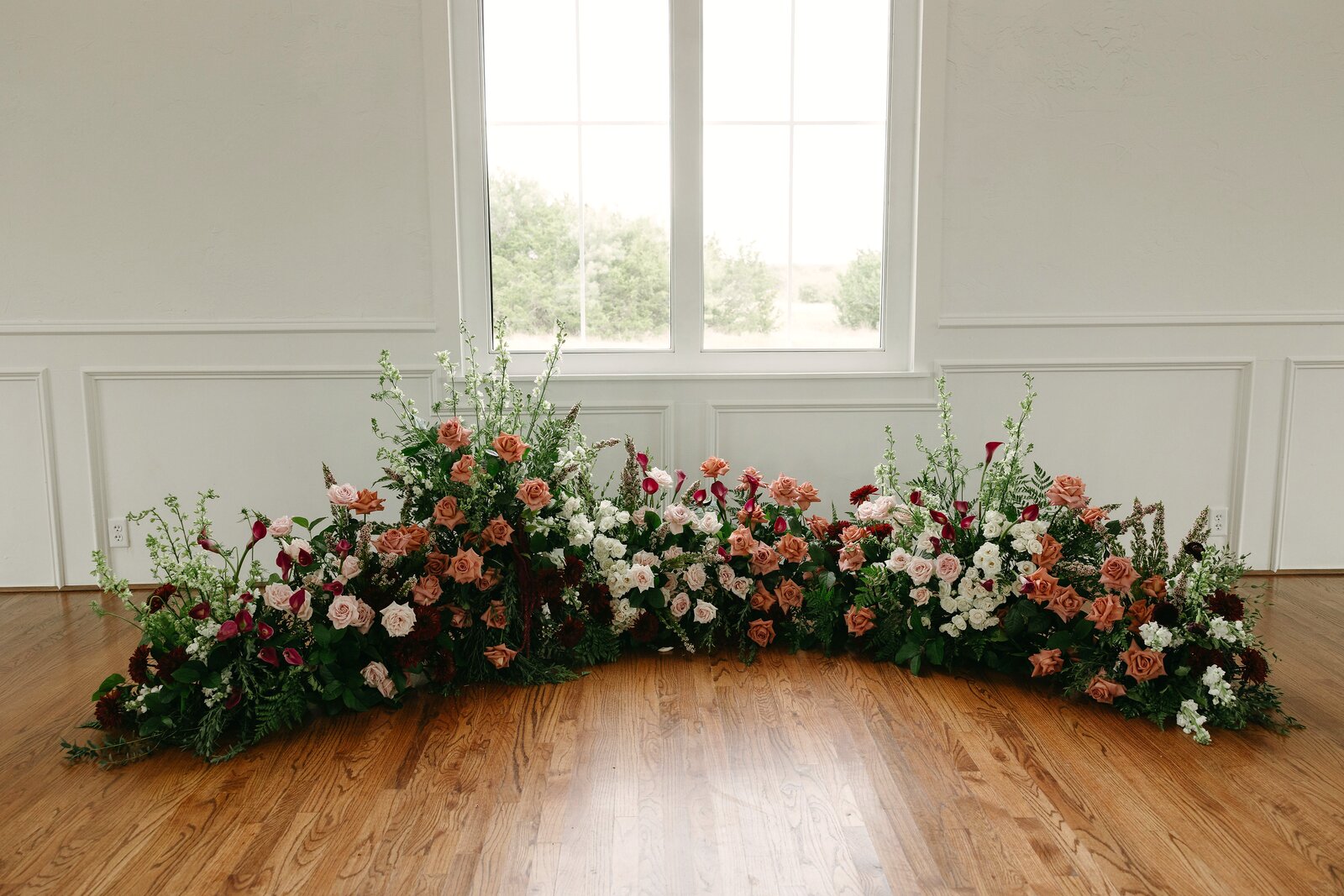 Sweeping ground arc of dusty pink, burgundy, and white roses against tall white windows at Parker Manor by B.blumen