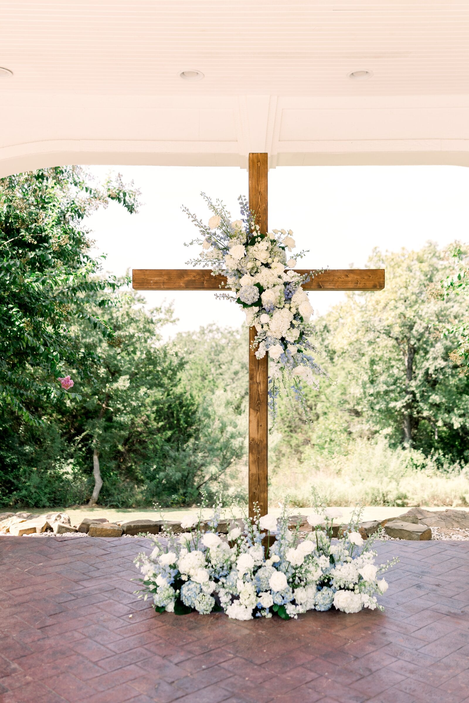 Tall wooden cross under the Parker Manor pavilion with cascading blue, white, and lavender florals at its base by B.blumen