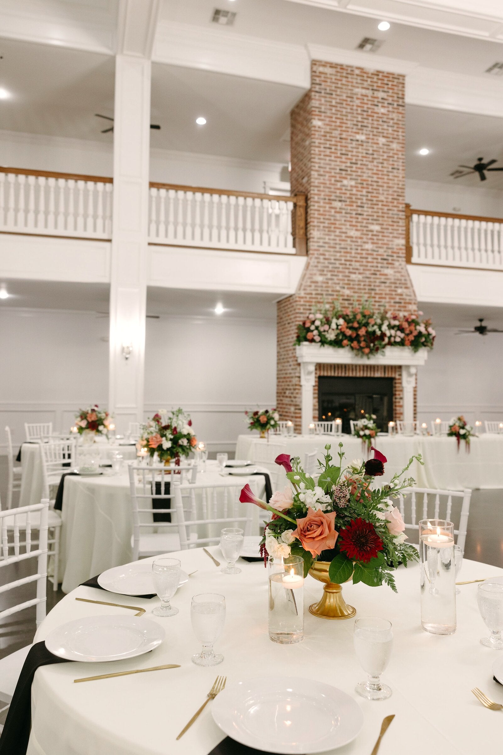 Reception hall at Parker Manor with three-story brick chimney rising past the balcony, round tables with autumn florals and chiavari chairs by B.blumen