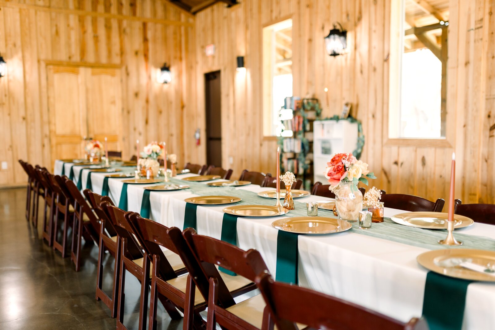 Long reception table at Westwood Hall with white centerpieces, teal sashes, gold chargers, and clustered candles, set against warm wood walls by B.blumen