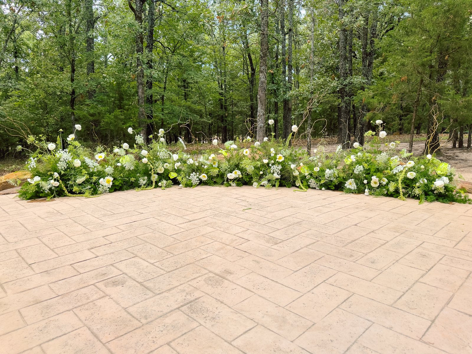 White and green ground floral installation at The White Sparrow ceremony, a low line of white blooms and greenery against the trees, by B.blumen