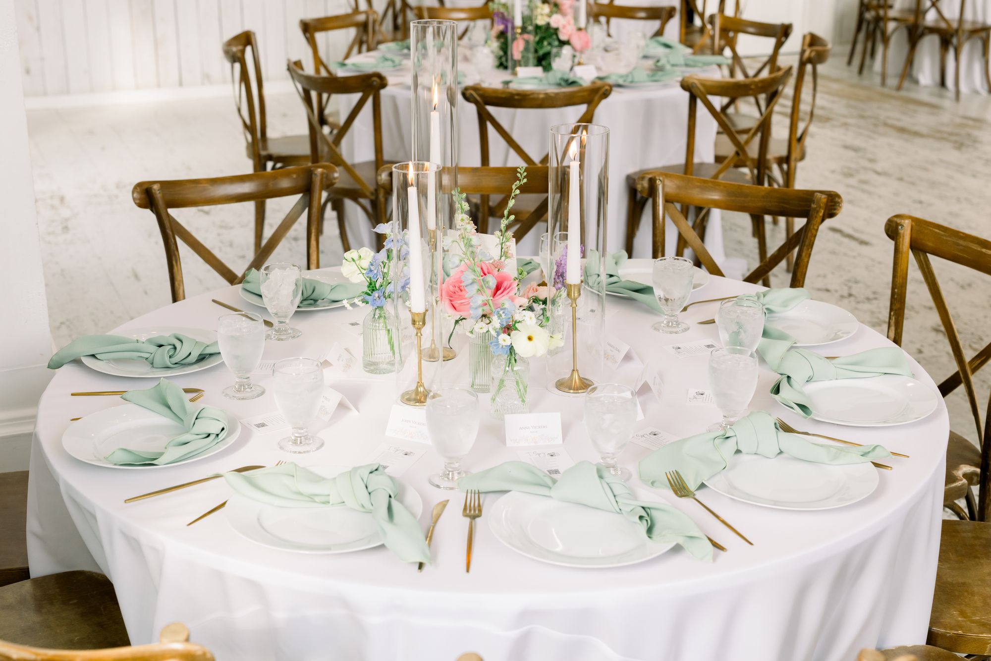Round reception table at The White Sparrow with a low blush-and-white centerpiece, sage napkins, and cross-back chairs, by B.blumen