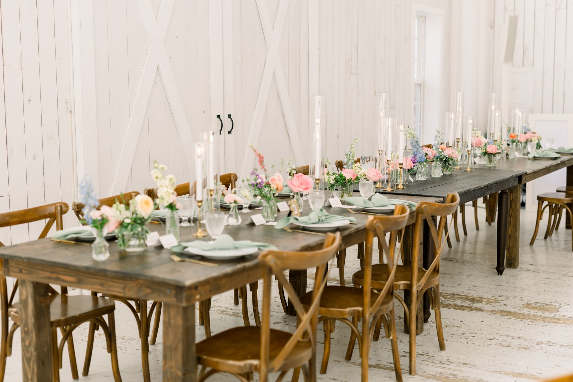 Long head table at The White Sparrow with a greenery runner, taper candles, and place settings down the run, cross-back chairs along both sides, by B.blumen