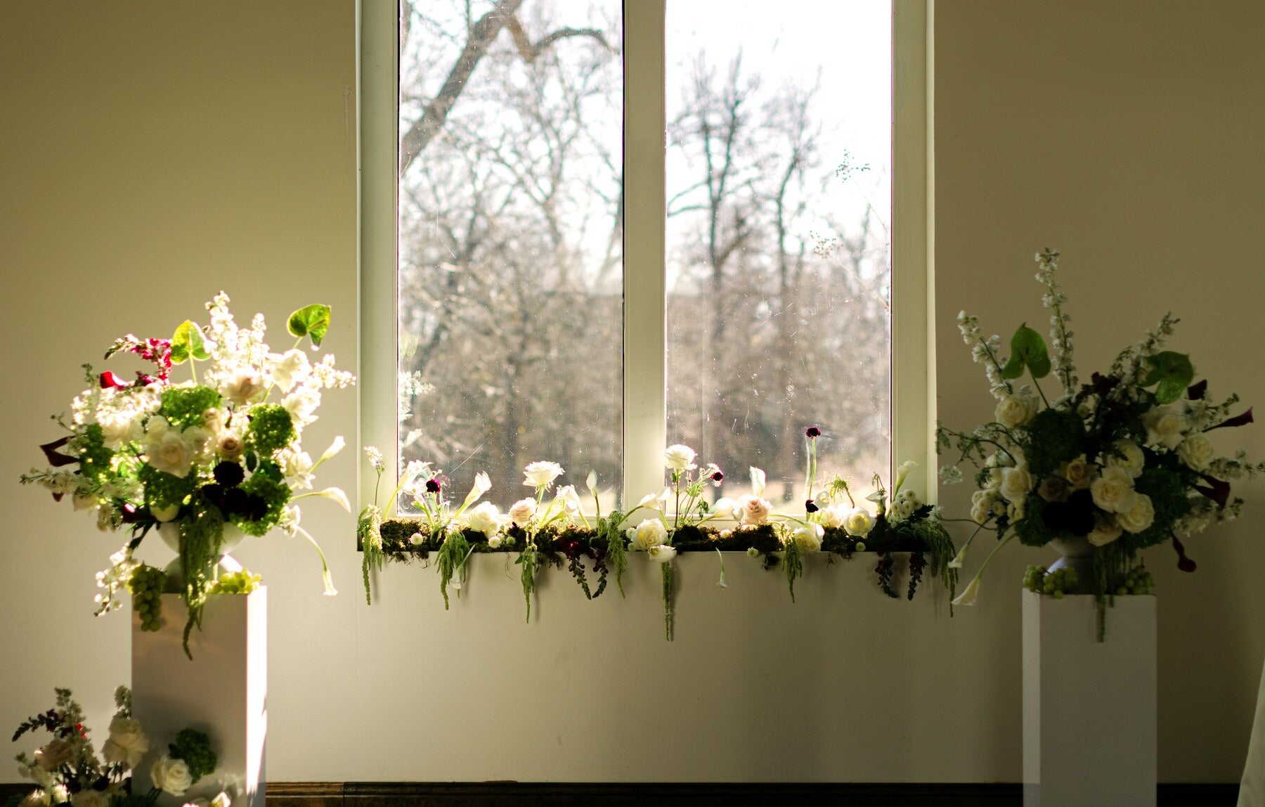 Pedestal floral arrangements flanking the arched windows of The Springs Waxahachie chapel by B.blumen
